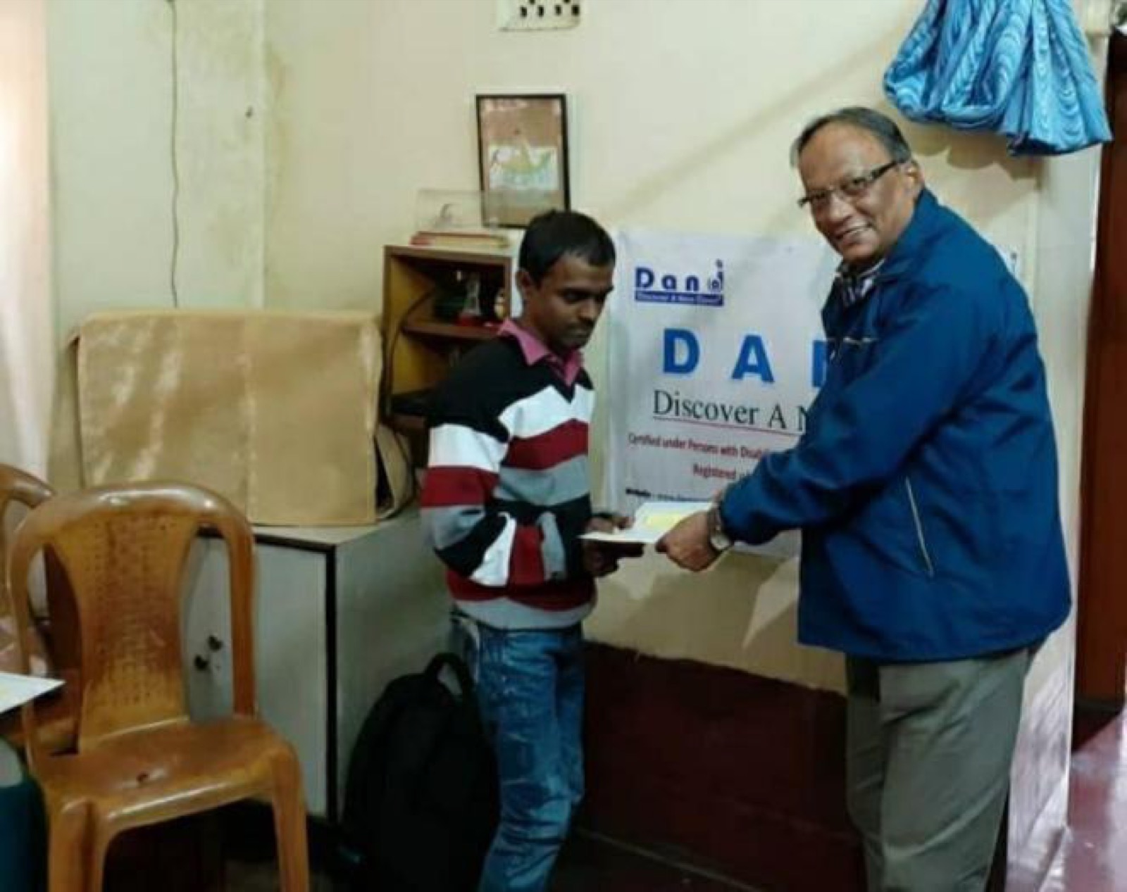 A DAND supporter presents a First Step grant to a young man in the DAND office.